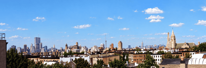 Panorámica de un paisaje urbano con edificios altos, bajo un cielo azul con nubes esponjosas.