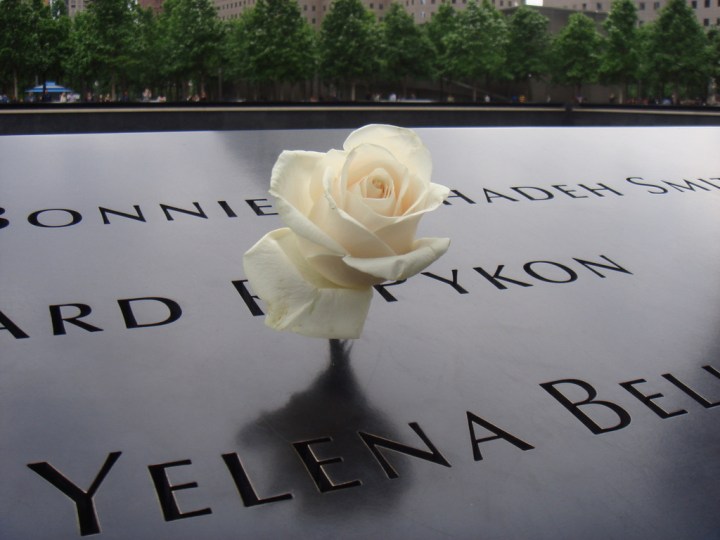 Una rosa blanca reposando sobre una placa con nombres en un monumento conmemorativo.